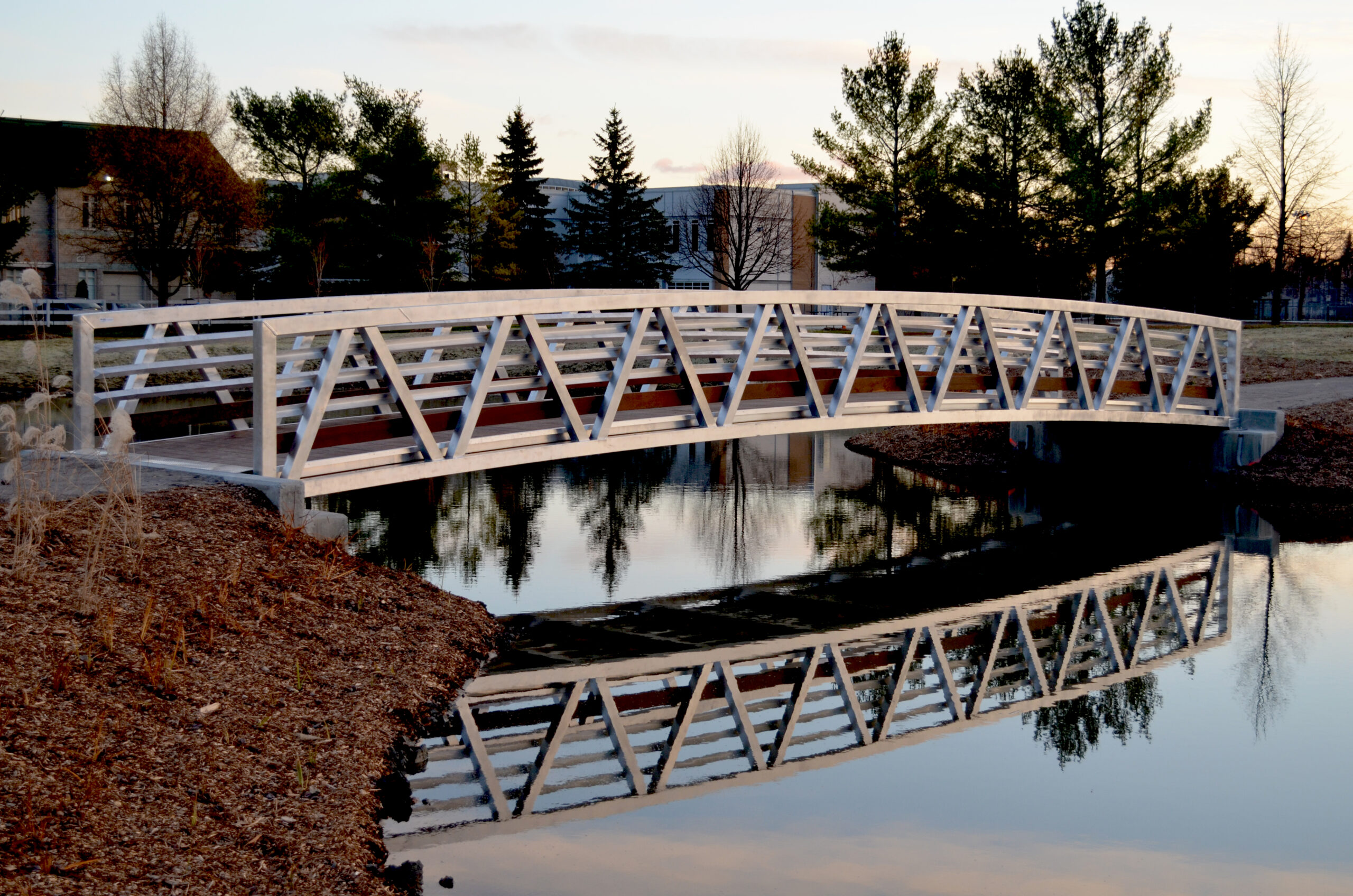 Custom pedestrian bridge with hardwood decking over pond in Quebec, Canada