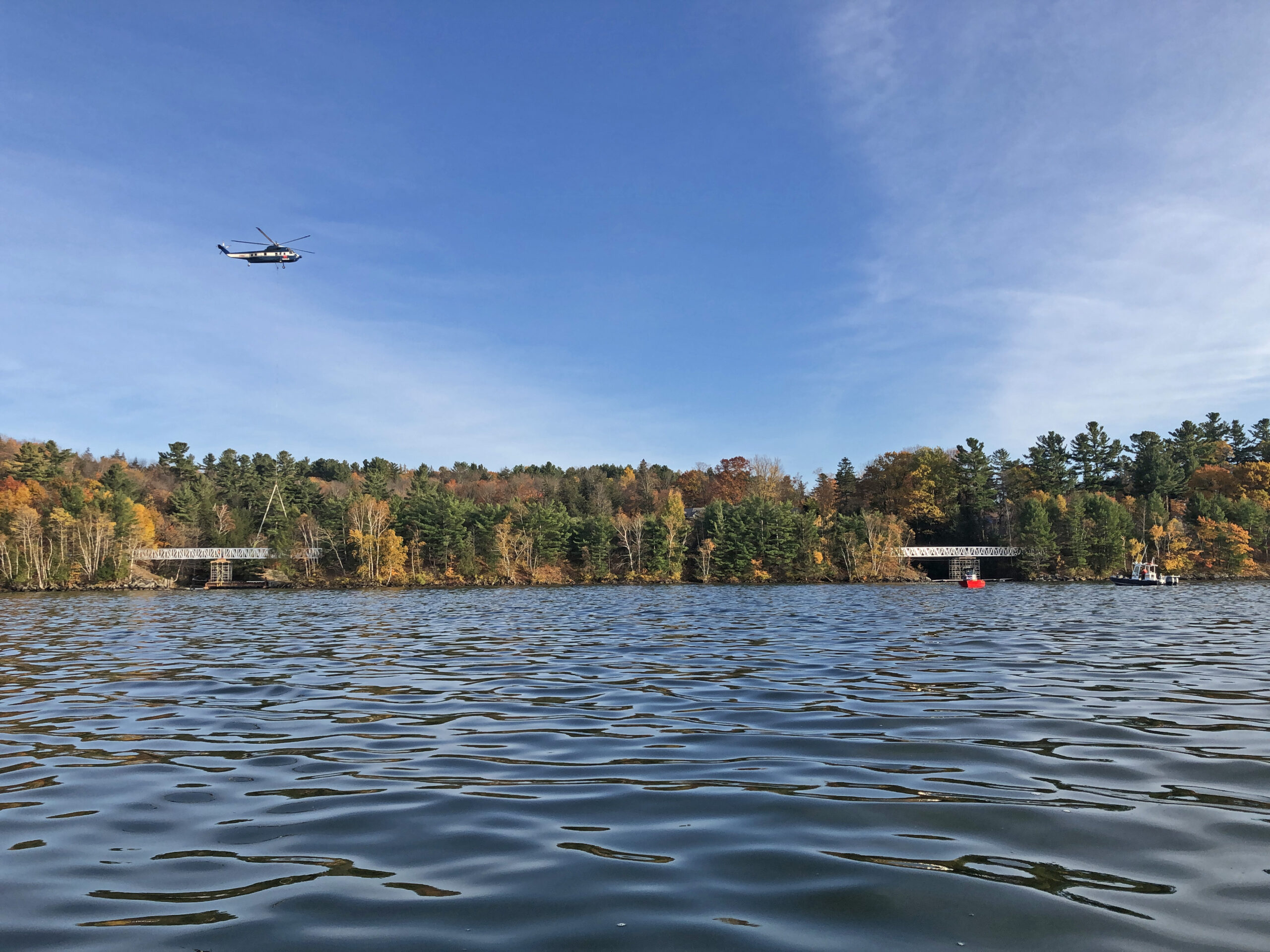 Helicopter lowering aluminum pedestrian bridge into place over a lake in Canada