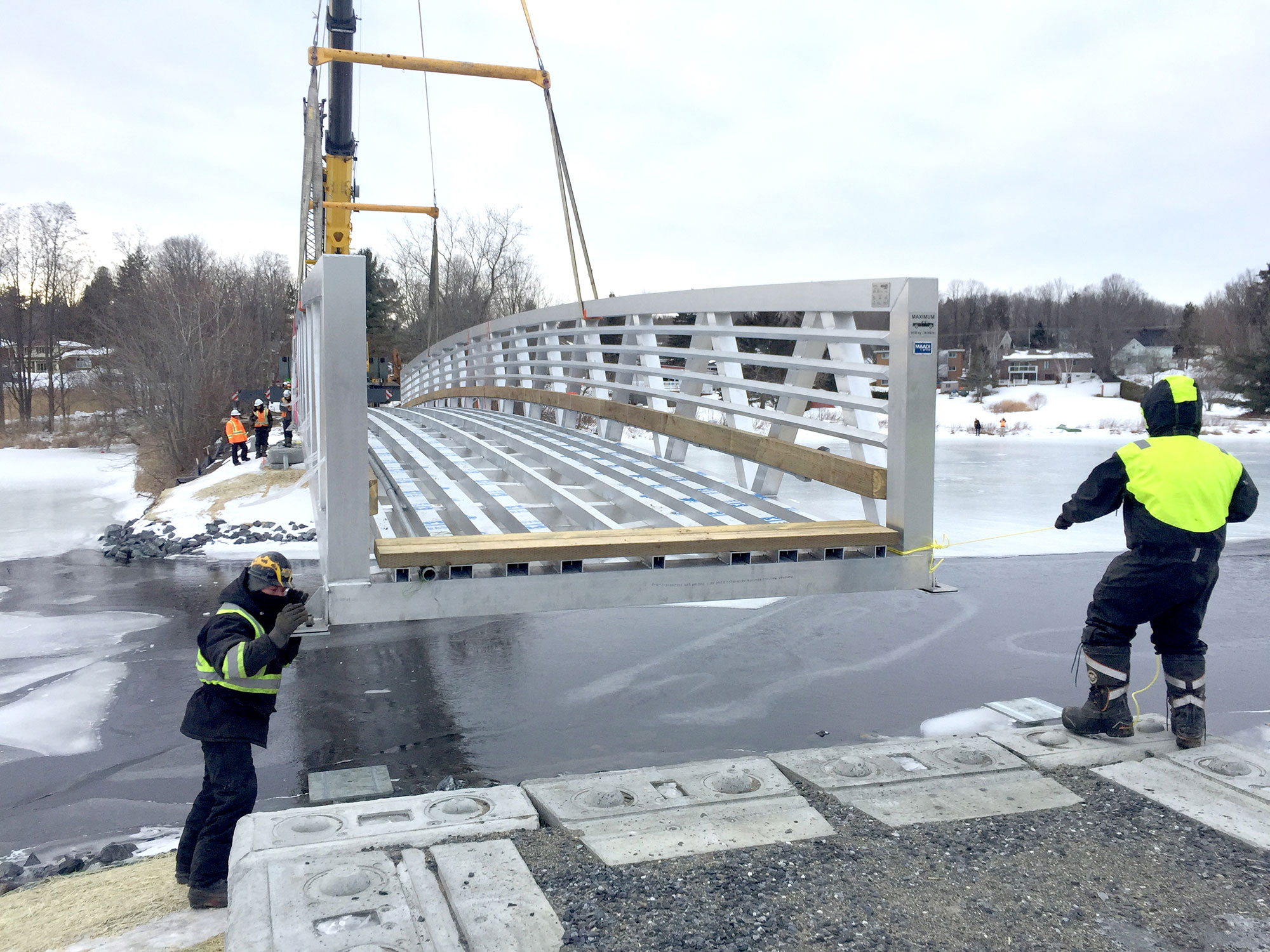 Prefabricated custom footbridge being lowered into place by crane in icy winter conditions