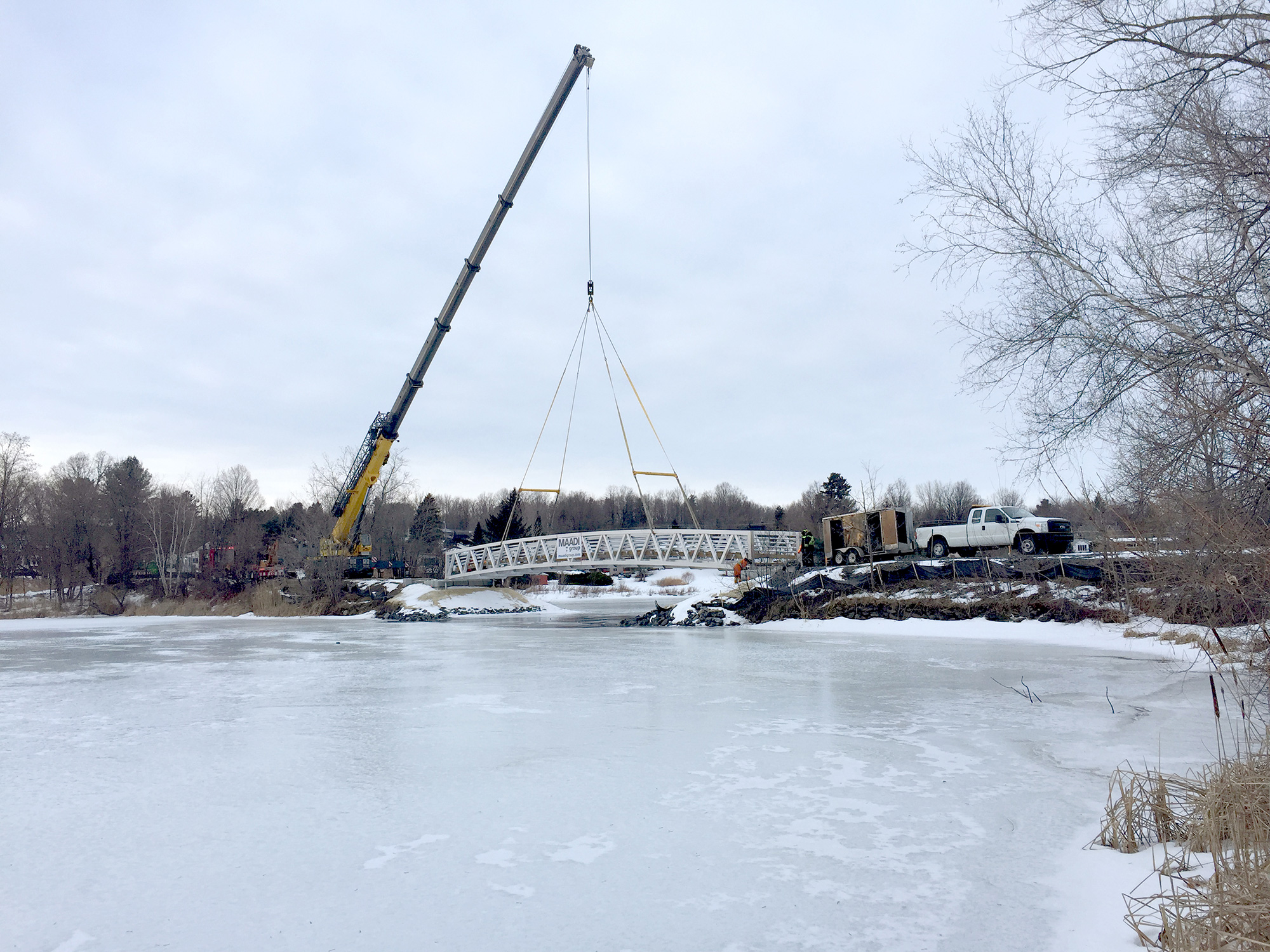 Prefabricated custom footbridge being lowered into place by crane in icy winter conditions
