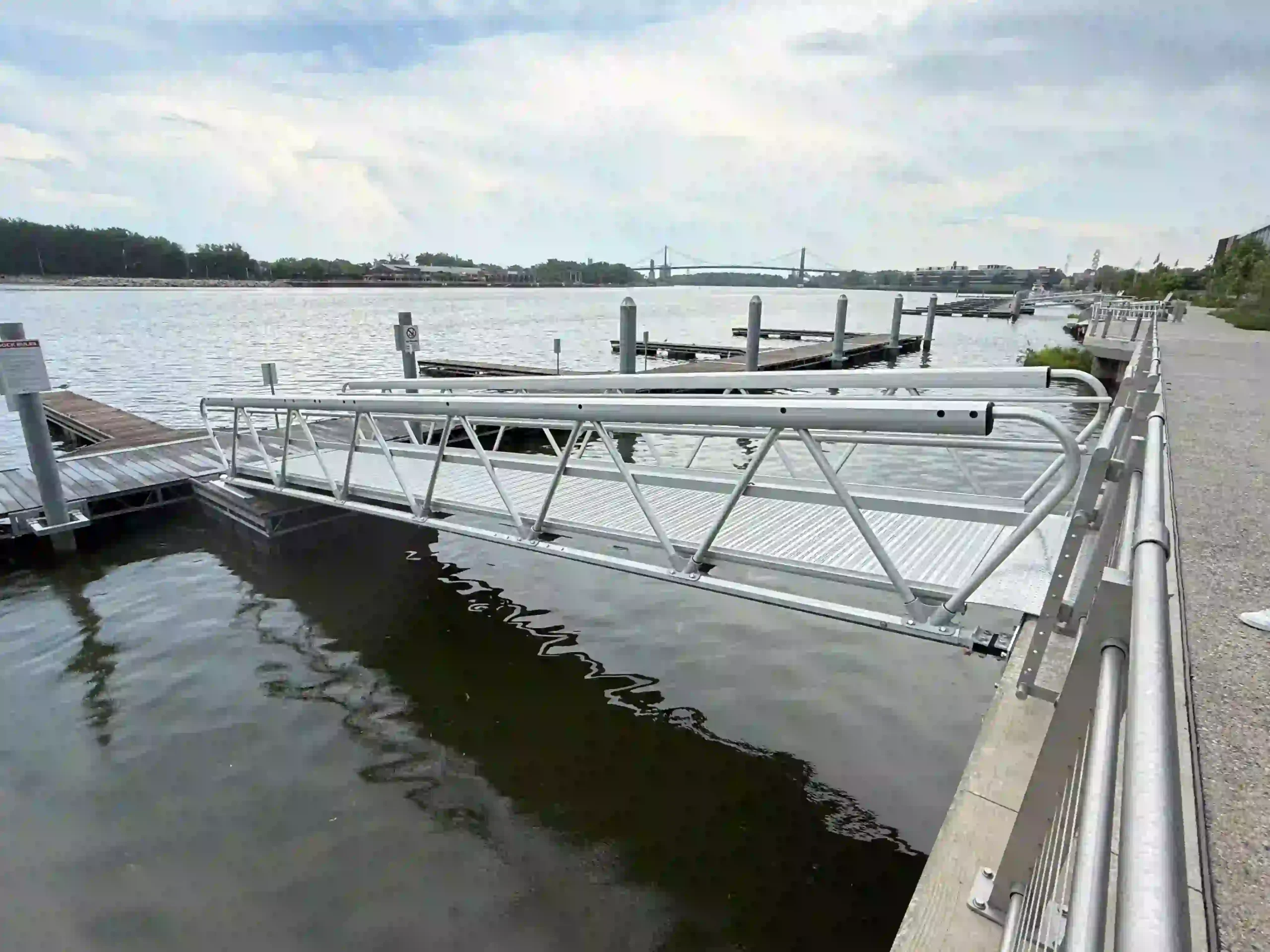 Aluminum truss gangway with handrails connecting shore to a floating dock.